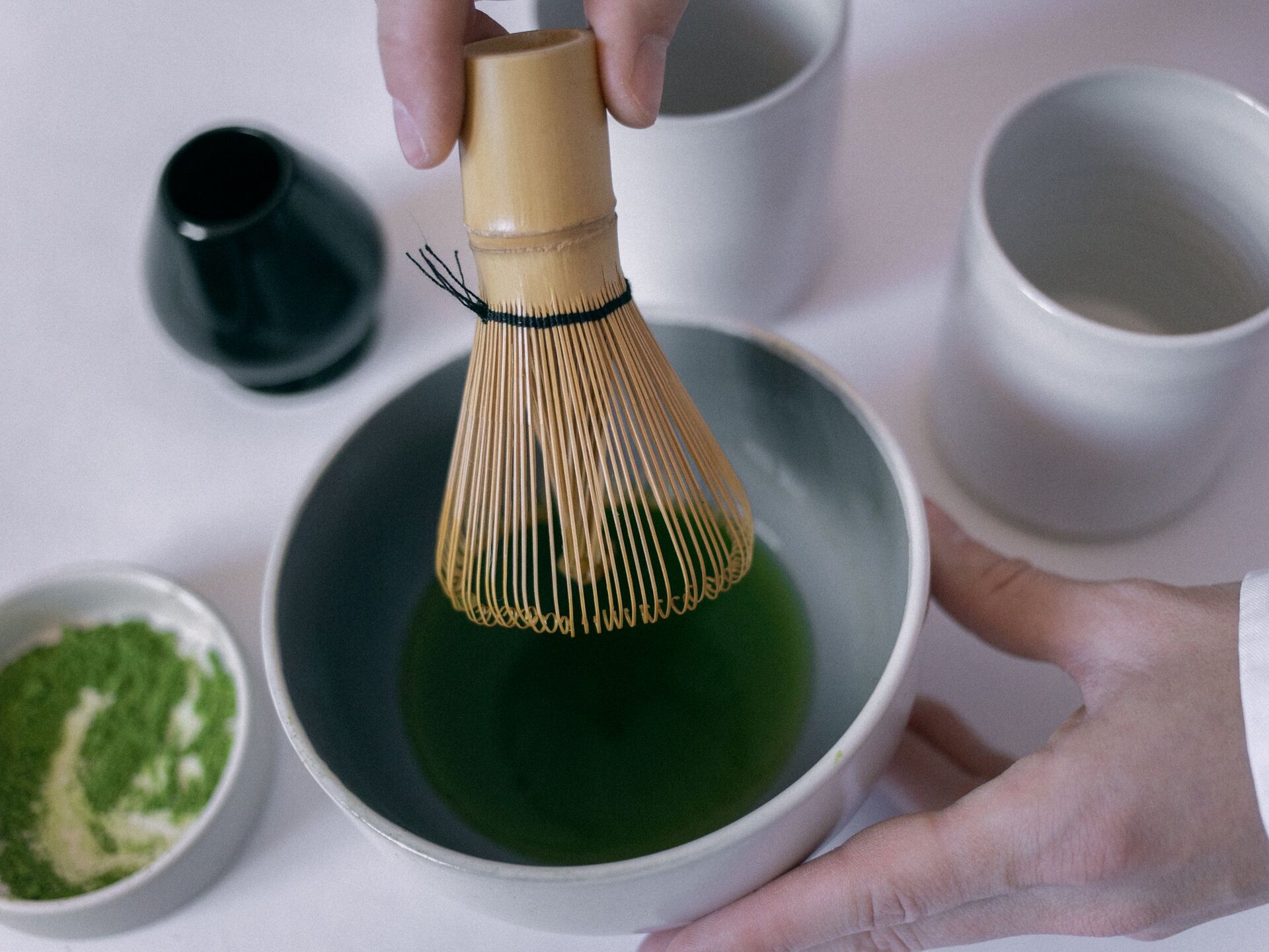 Mains fouettant un matcha avec un fouet en bambou dans un bol en céramique