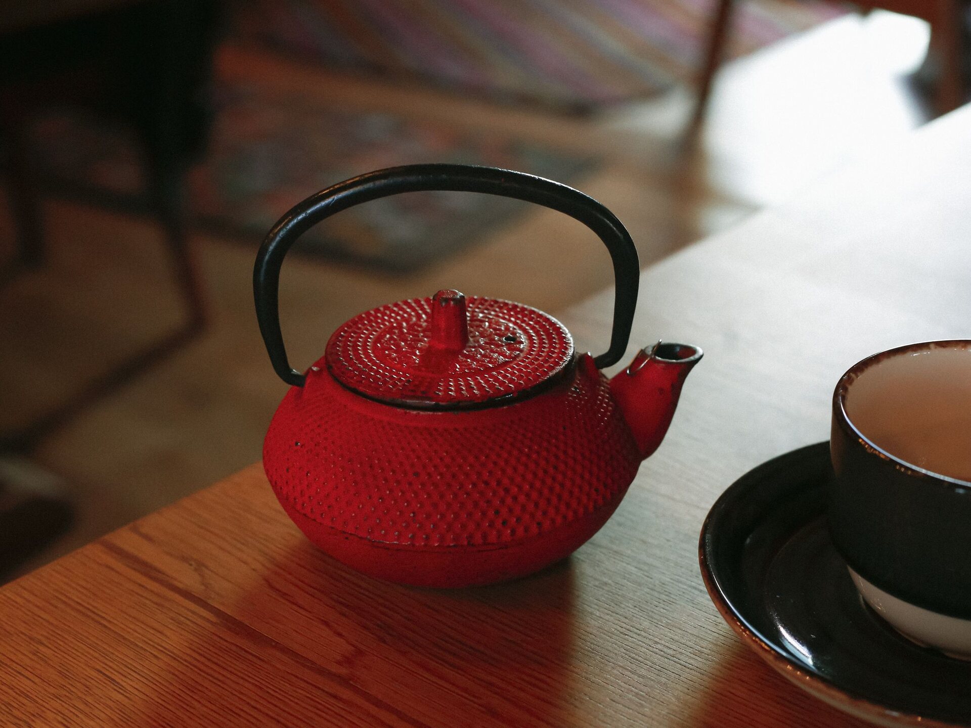 Théière en fonte rouge à côté d'une tasse en céramique sur une table en bois